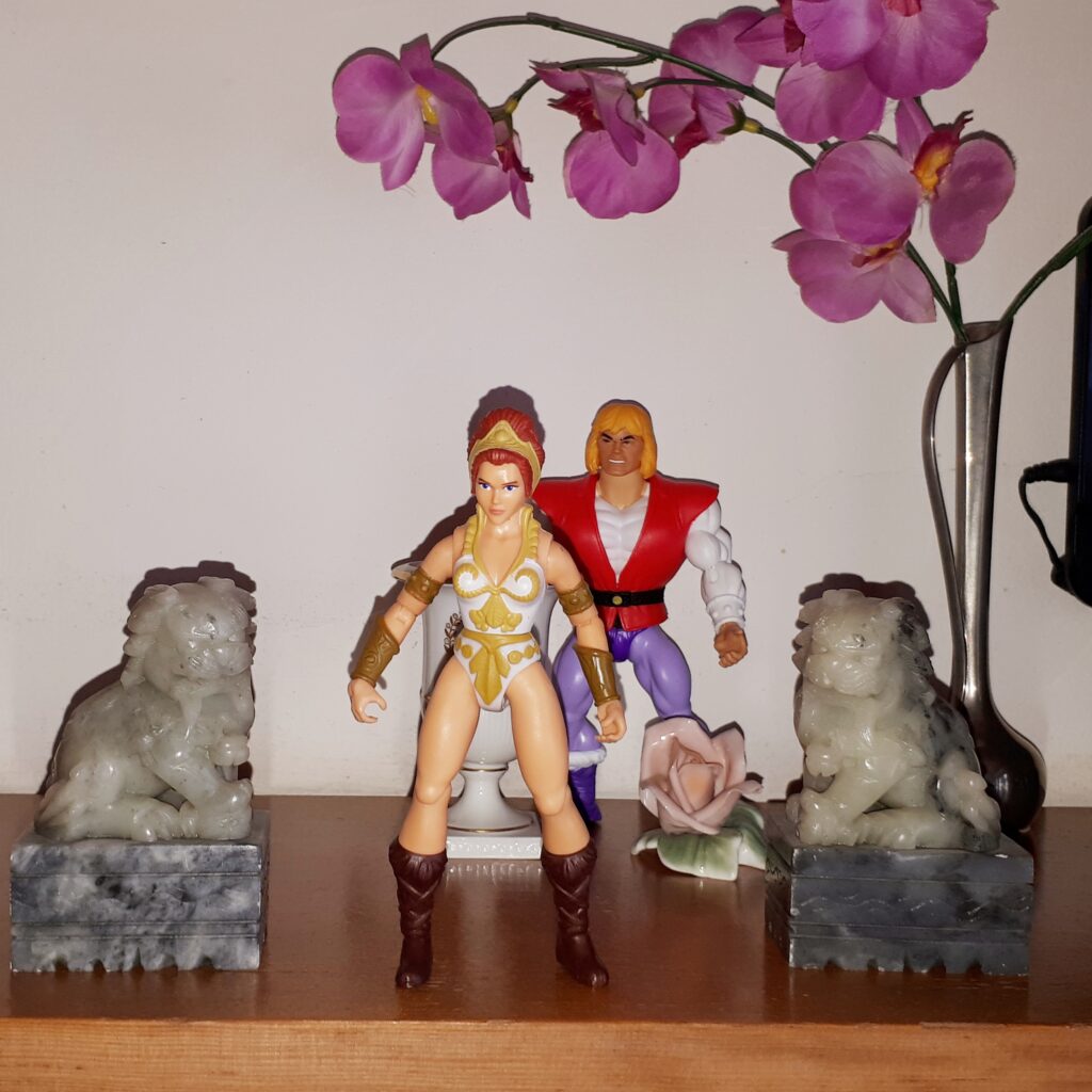 Teela is sulking in the palace garden, while Adam looks on.
