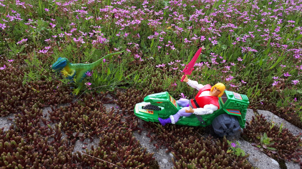 Adam is riding the Road Ripper, while a Raptor appears in the grass.